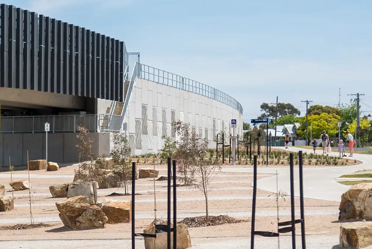 People walking on paths through gardens near a train station