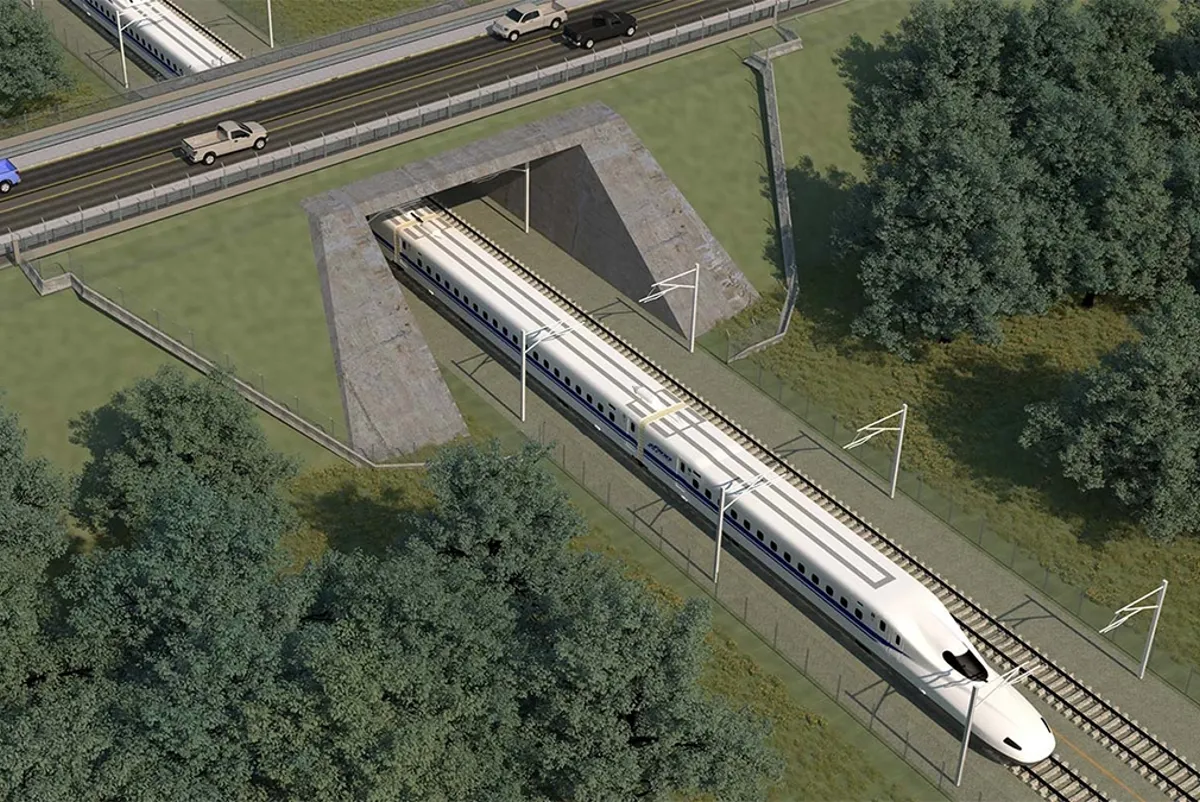A high-speed train traveling under a highway